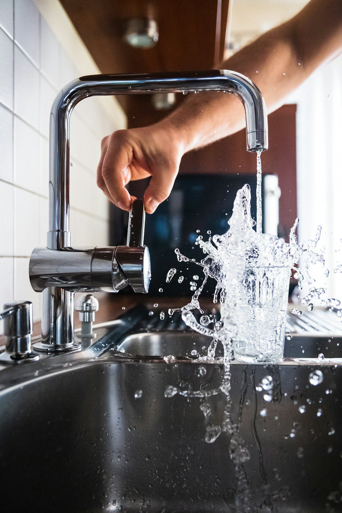 A hand turning on a kitchen tap with water running into the sink